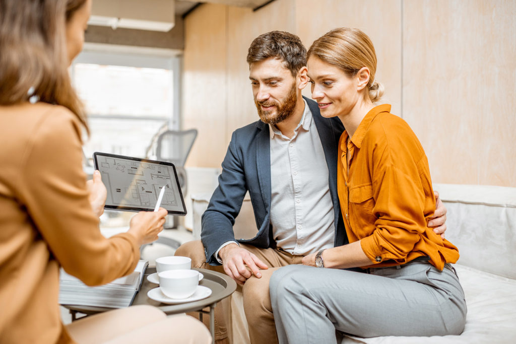 Young and lovely couple choosing a new house to buy, looking on the projects with a sales manager in the office of real estate agency