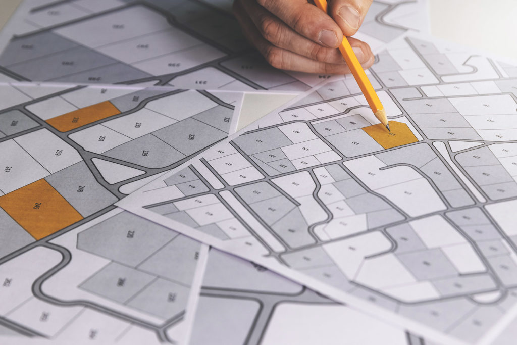 hand with pencil on cadastral map - choose and buy a building plot for house construction